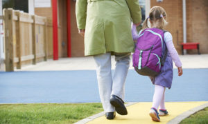 mother and daughter seen from behind walking to school and holding hands