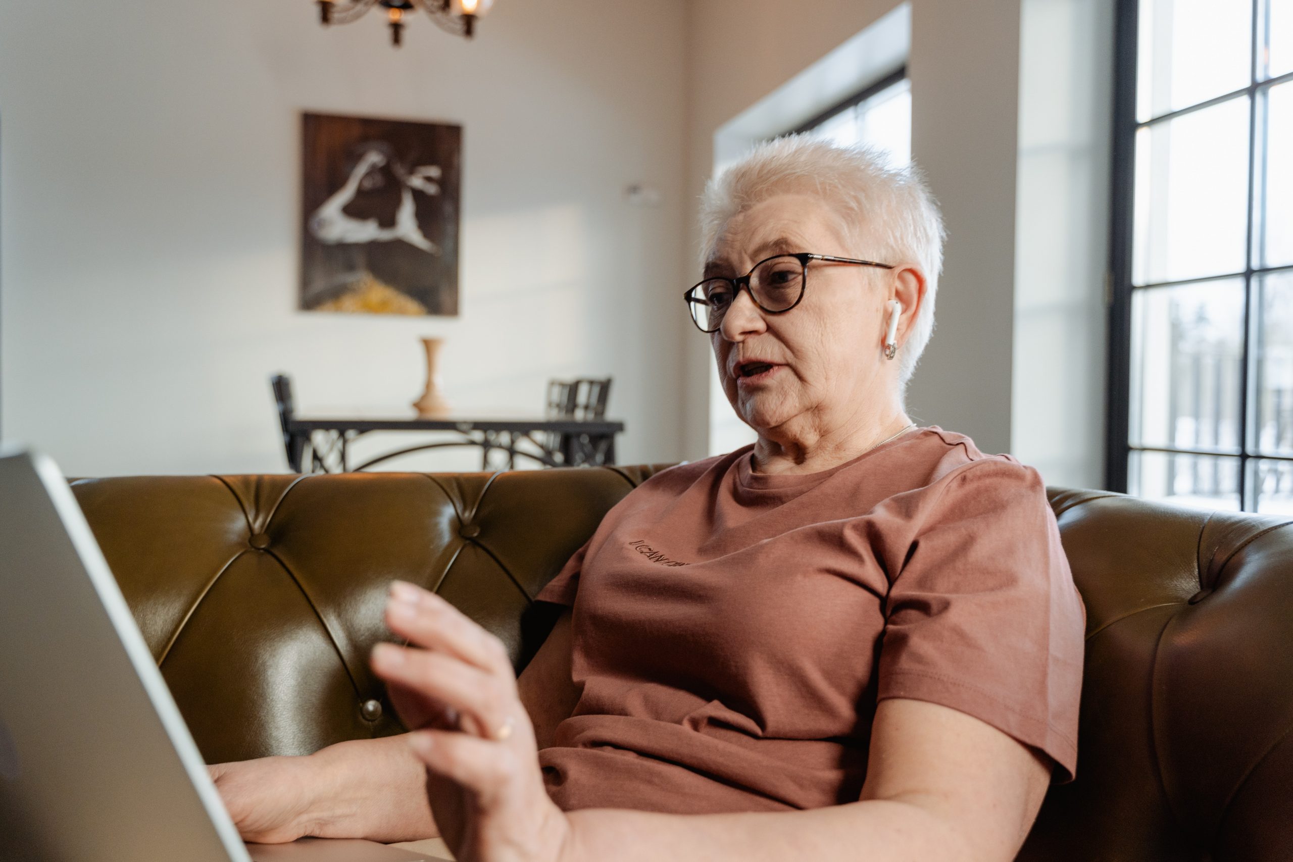 grandmother sitting on a couch in her living room on the laptop for aphasia therapy